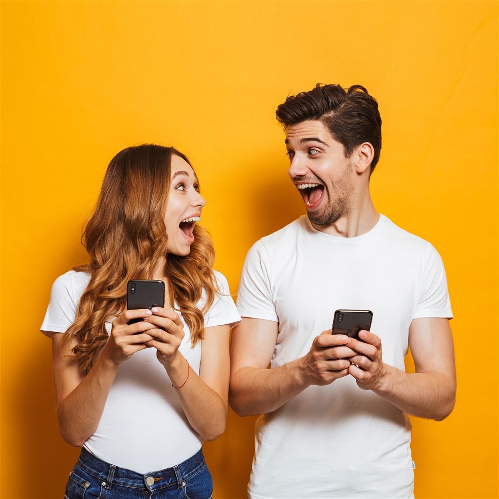 En mand og en kvinde holder hver sin mobiltelefon og ser meget begejstrede ud
