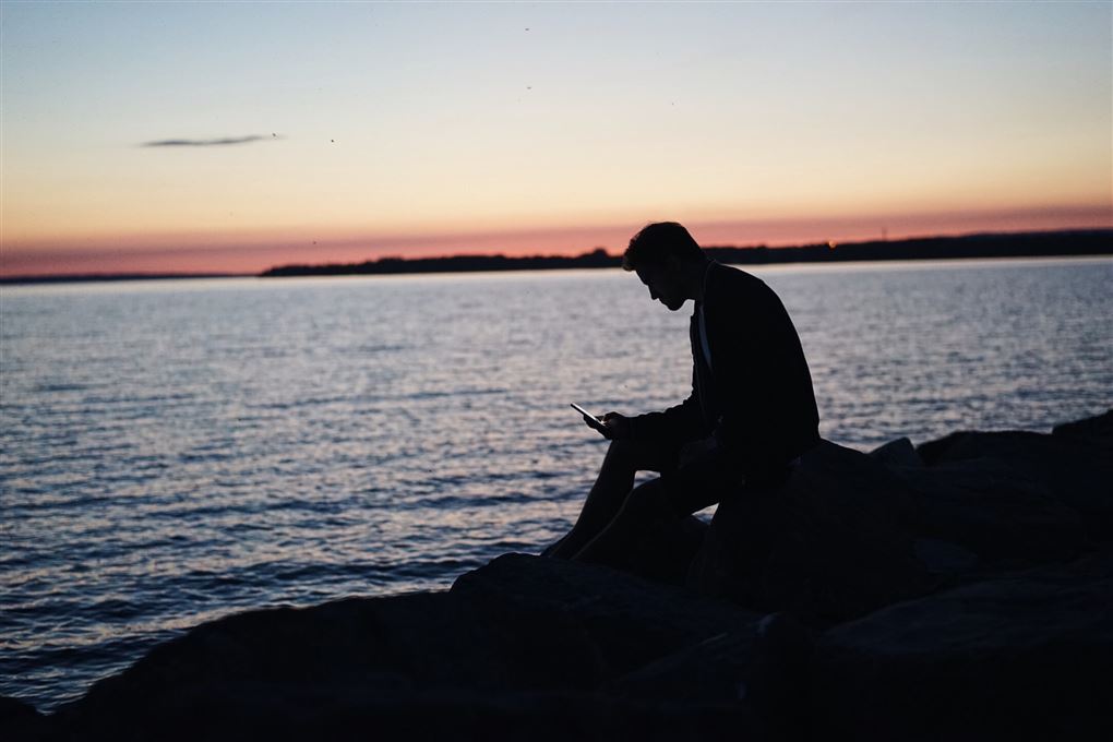 En mand sidder i solnedgangen og stirrer på sin telefon