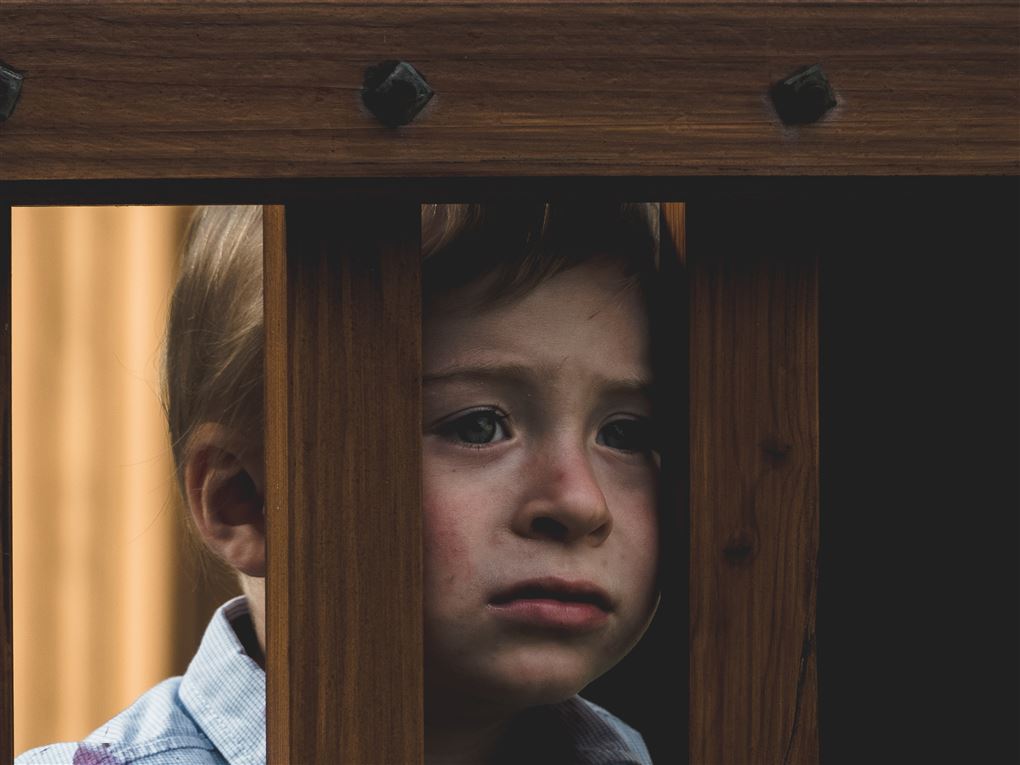 En trist dreng kigger ud af en tremmseng