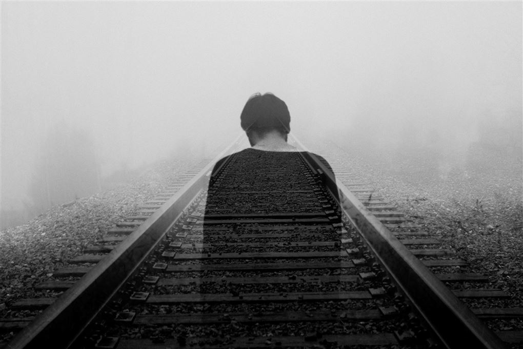 En mand kigger trist ned på nogle jernbanespor