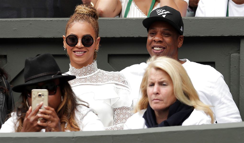 Beyoncé og Jay Z til en tenniskamp. De er begge klædt i hvidt og hun har store solbriller på.