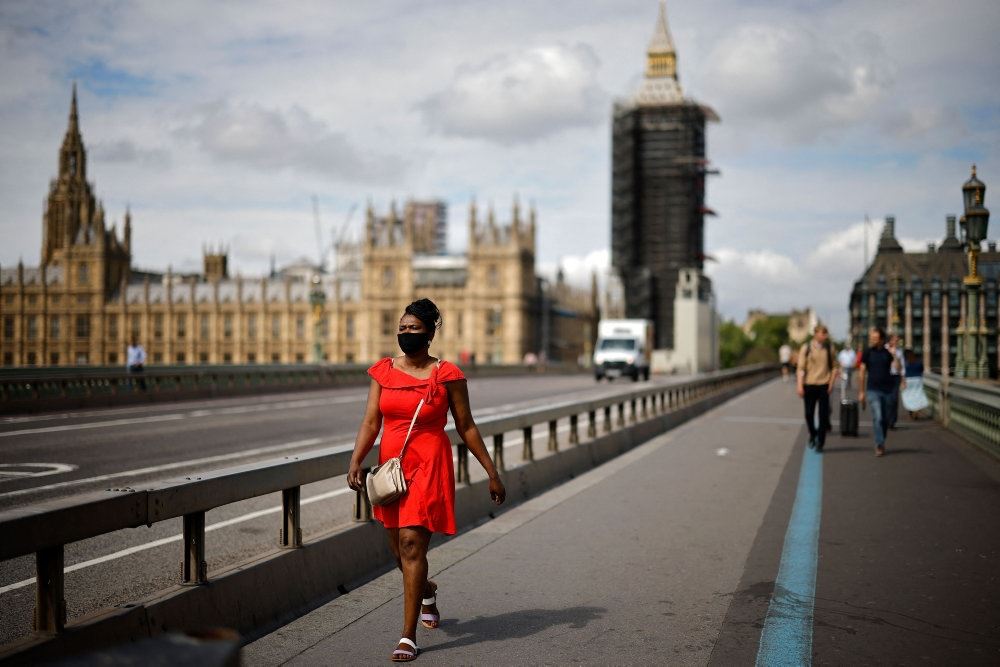 En mørk kvinde i rød kjole går på en bro med Big Ben i baggrunden