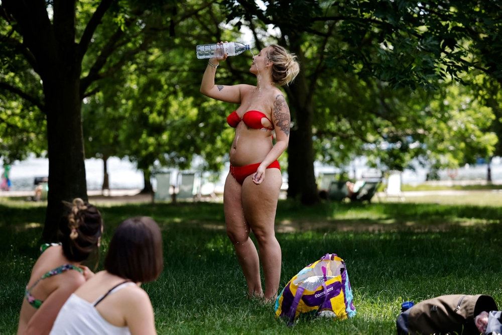 Eb kvinde i bikini i en park hun hælder koldt vand ud over sig.