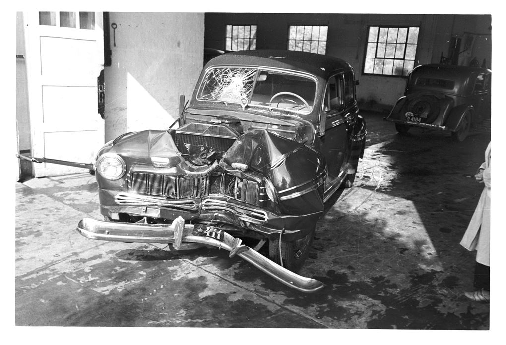 Et sort/hvid foto af den skadede bil. Fronten er helt bulet ind og forruden er smadret i passagersiden. 