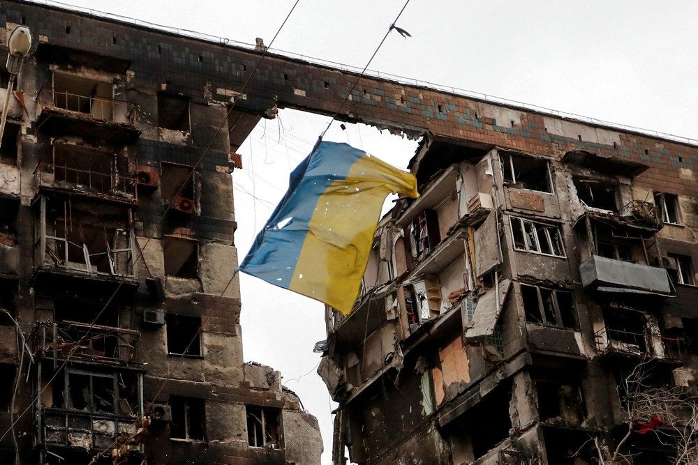 ukrainsk flag foran en ødelagt bygning