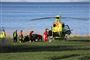 En redningshelikopter og redningsfolk ved en græsplæne ved havet