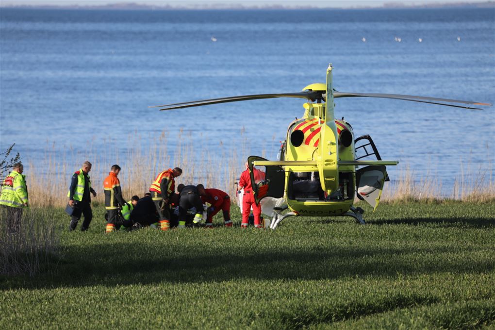 En redningshelikopter og redningsfolk ved en græsplæne ved havet