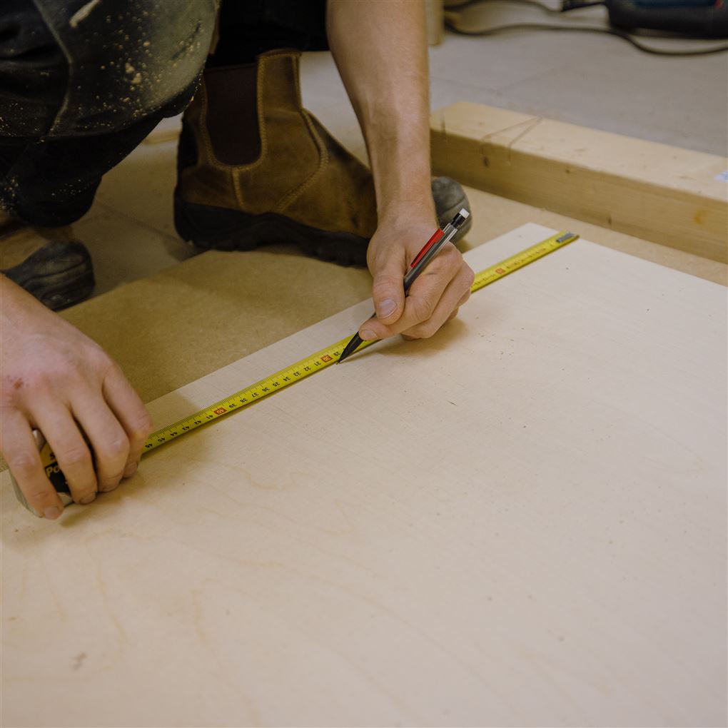 En håndværker måler op på et gulv. 
