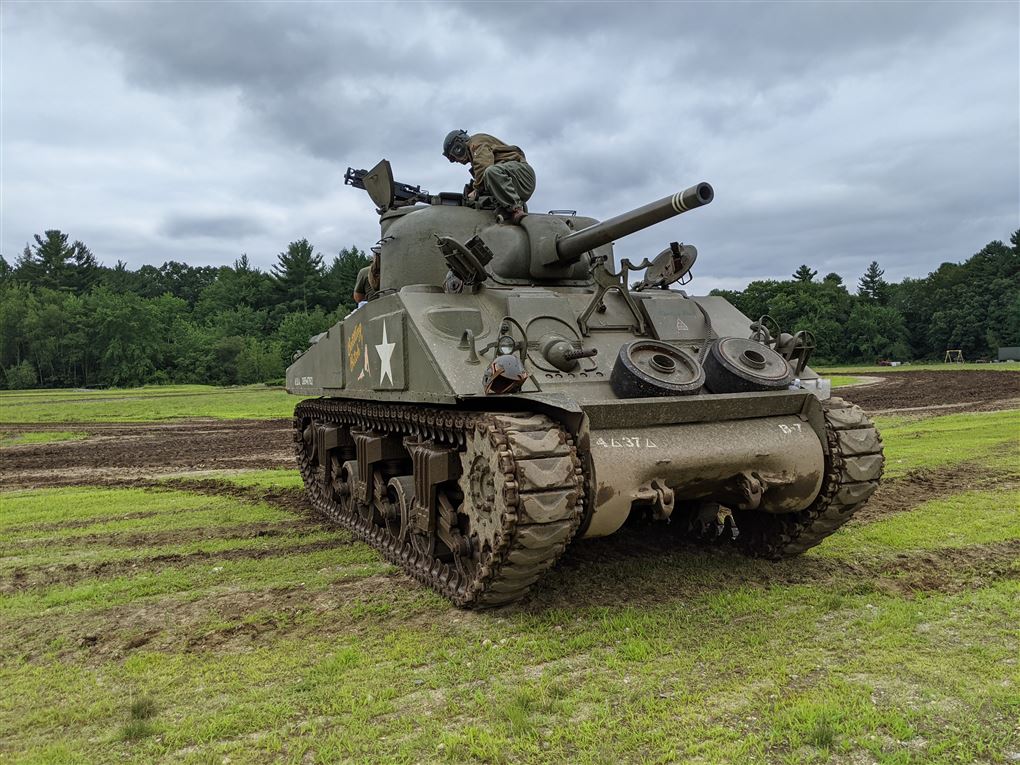 En tank på en plæne der er skov i baggrunden