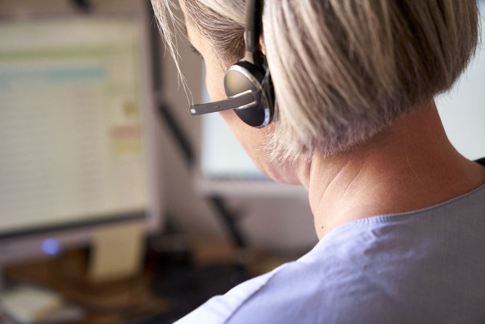 En kvinde med et headset på og en computer foran sig