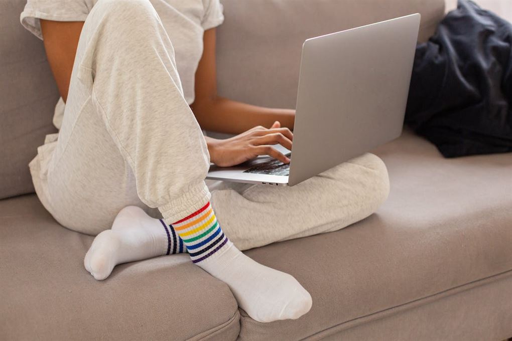 Kvinde i sweatpants sidder i sofa med computer