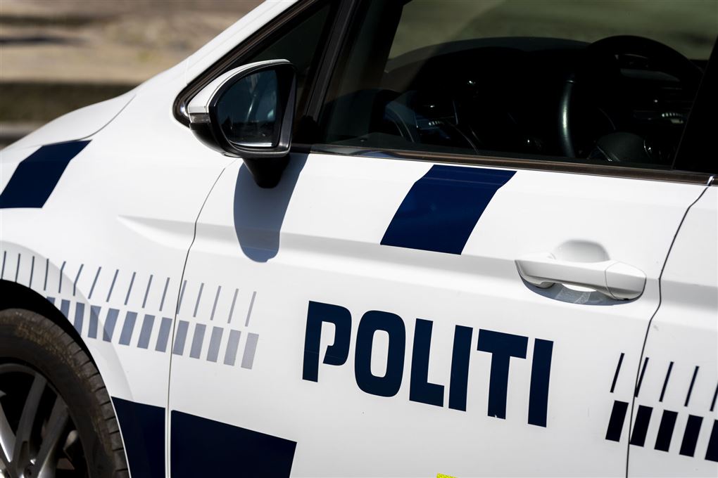 En politibil set fra siden. Den er hvid med blå skrift.