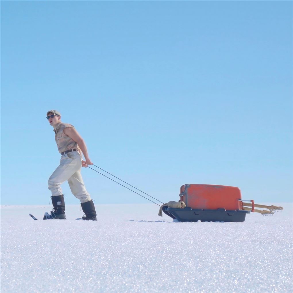 mand går på is med kuffert på slæde 