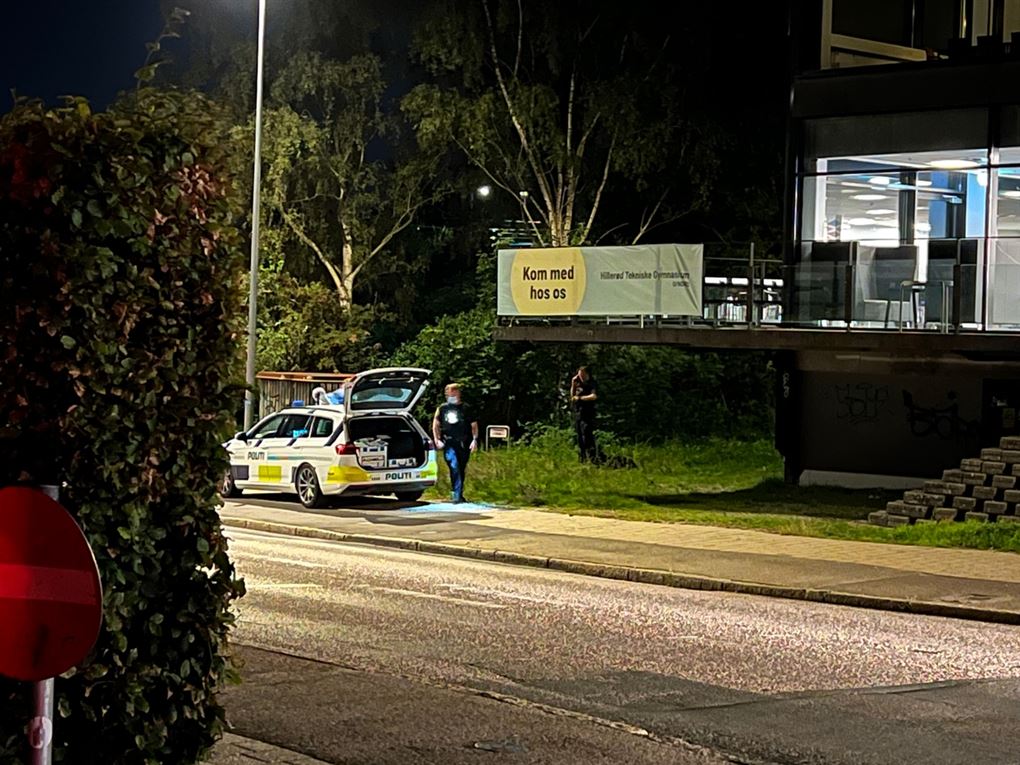 En politibil på en vej der går betjente rundt