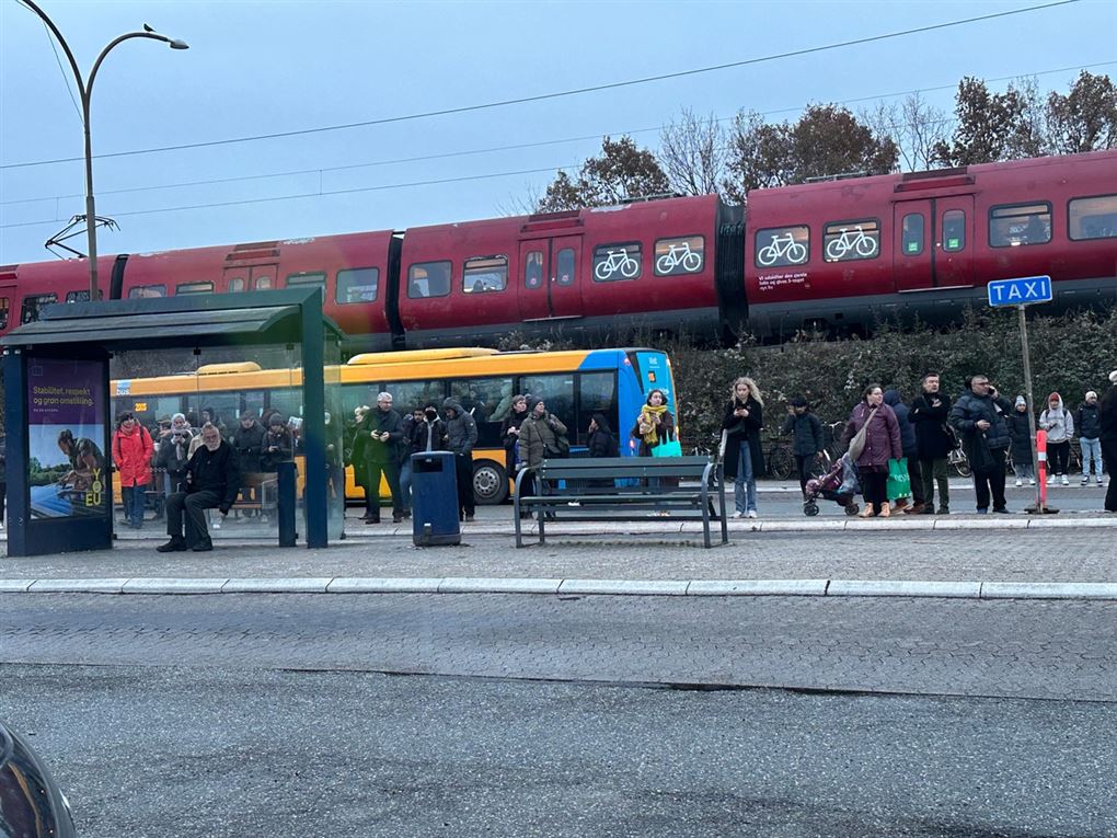 Foran en station med mange mennesker og et tog, der holder stille
