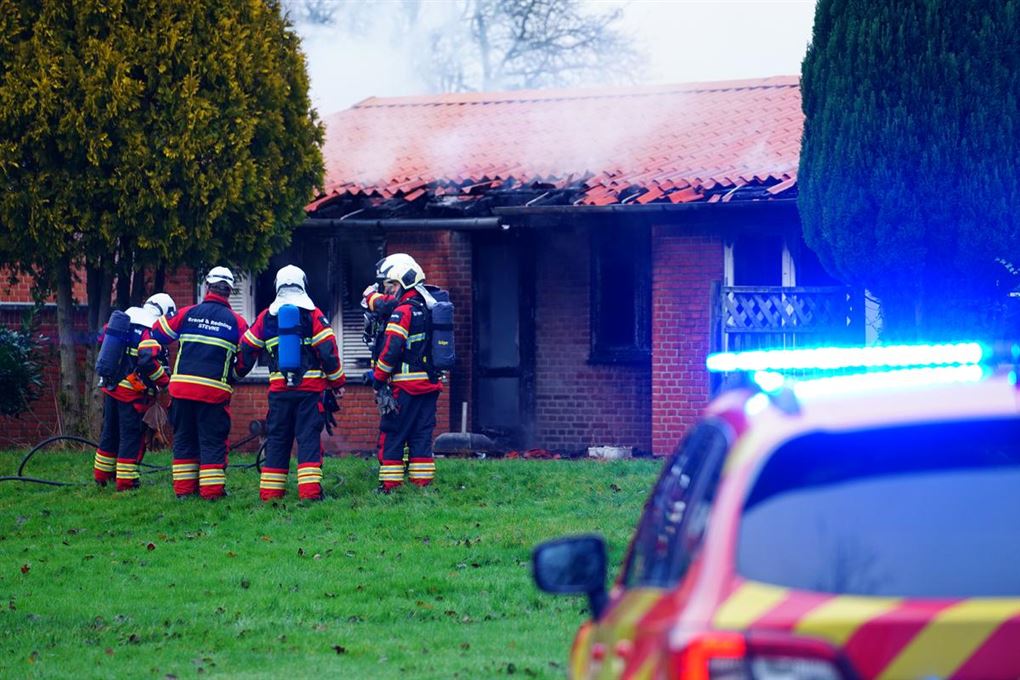 Fire brandmænd står foran den rygende bolig