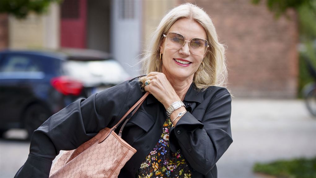 Smilende kvinde med solbriller og en taske over skulderen