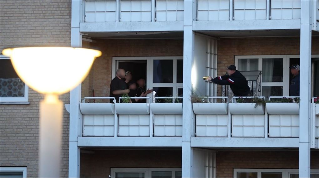 To altaner med personer på. På den højre altan står en mand med et skydevåben og sigter mod den venstre