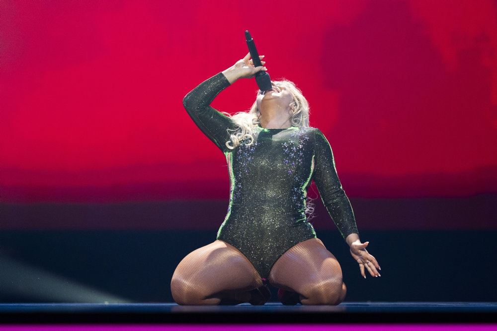 kvinde i sort bodystocking syngende på knæ på en scene