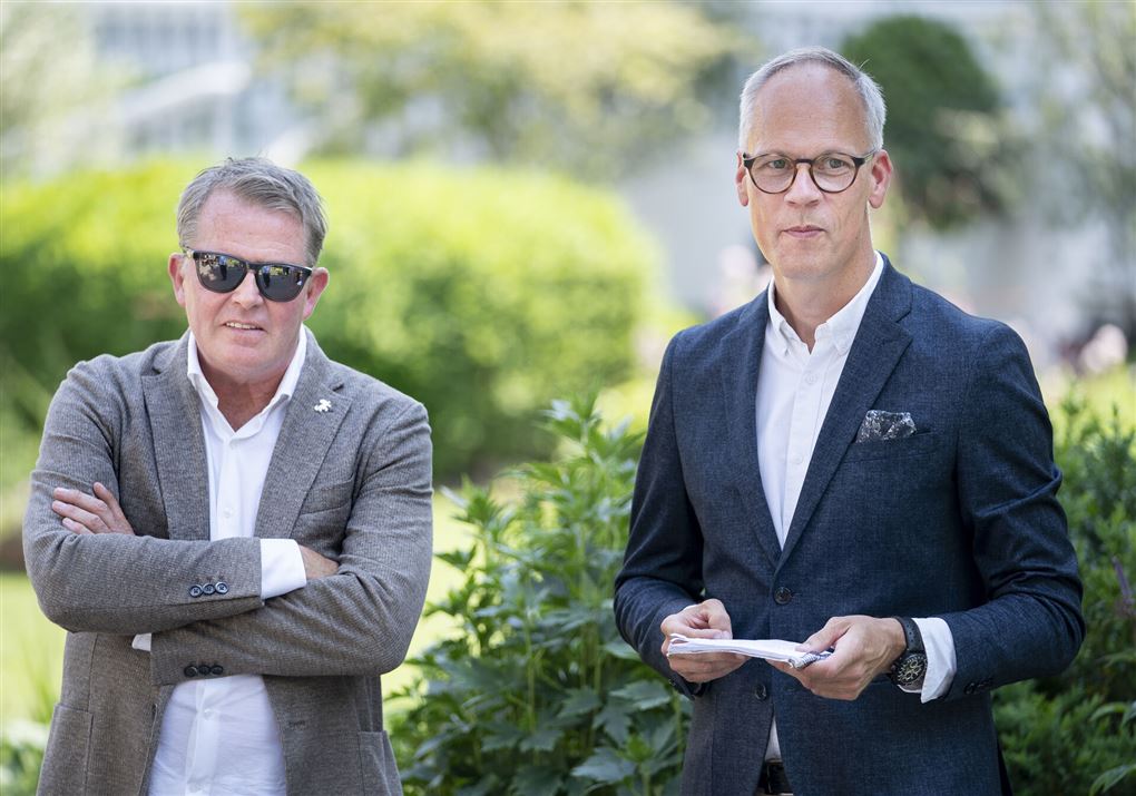 Mand med solbriller ved siden af man med papirer i hånden