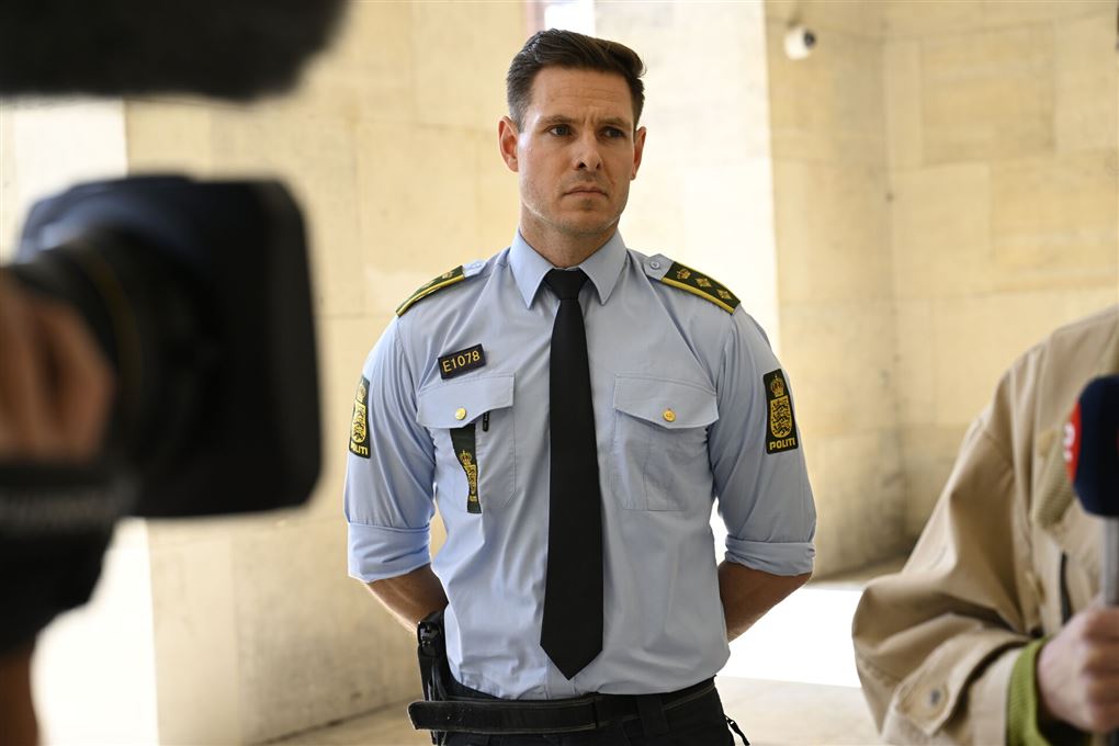 En politibetjent i uniform står foran et tv-kamera