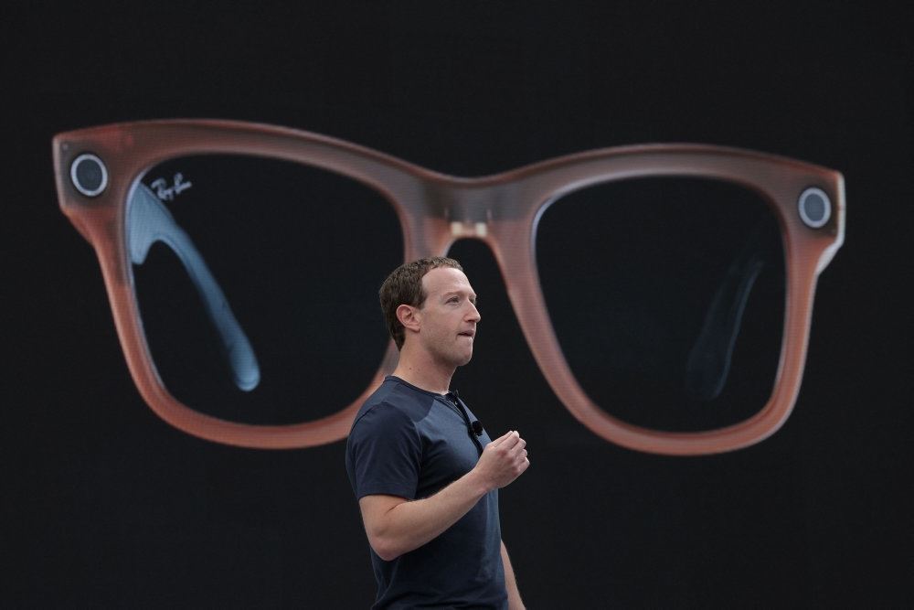 Mark Zuckerberg på en scene med billedet af et par kæmpe briller i baggrunden