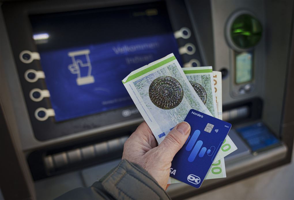 kontanter og kort i hånd på mand ved hæveautomat.