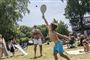 En mand og en dreng spiller strandtennis mens folk solbader