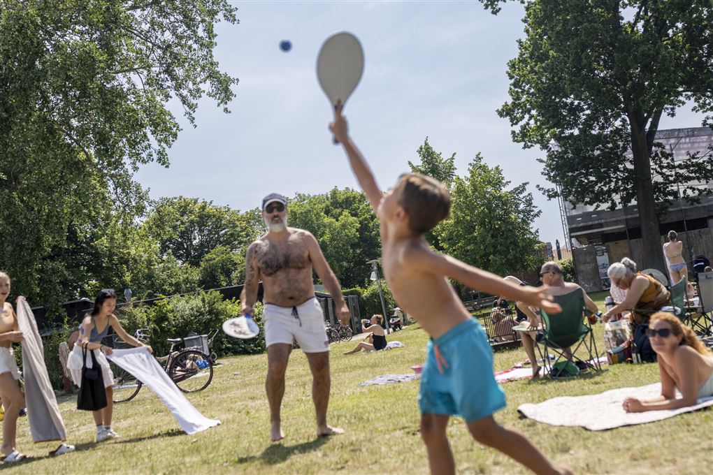 En mand og en dreng spiller strandtennis mens folk solbader