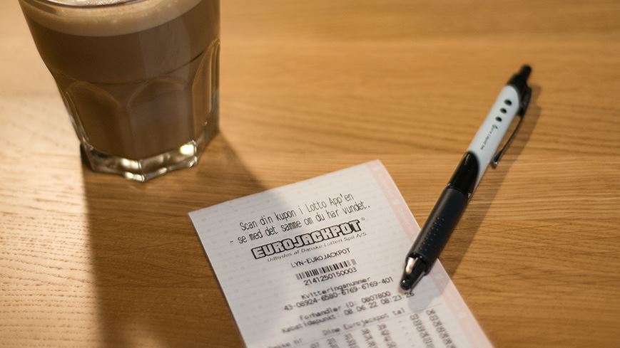 Lottokupon ved bord ved siden af fyldt kaffekrus