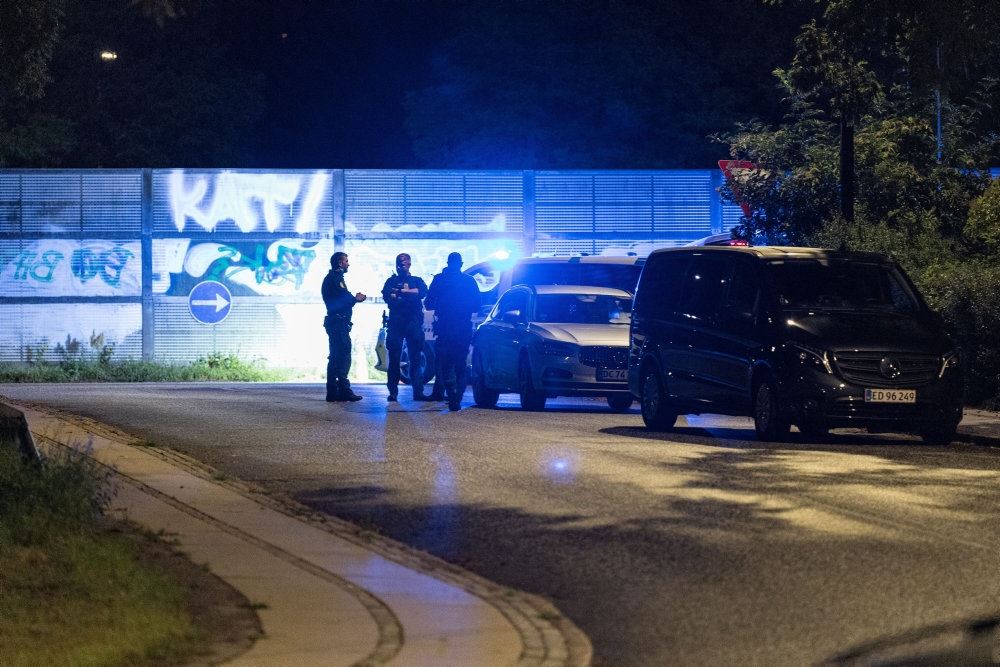 Politibetjente står i mørke ved siden af en politibil uden for en oplyst bygning