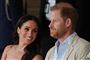 Meghan i sommerkjole læner sig smilende mod Harry i lys jakke og skjorte